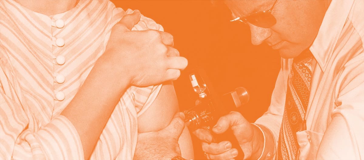 Woman lifting her shirt sleeve while a man inserts a medical shot into her arm