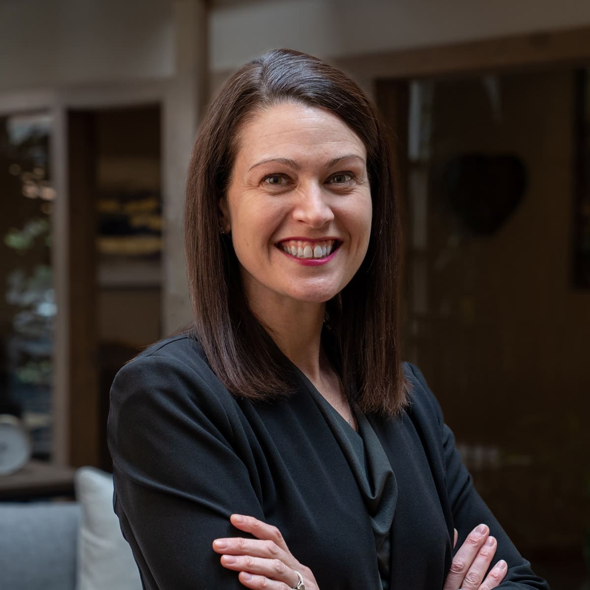 Headshot of a smiling young woman with dark brunette hair dressed in a blazer in front of a blurred background
